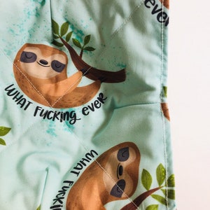 May include: A square, quilted pot holder with a light teal background featuring a cartoon sloth hanging from a branch. The text "WHAT FUCKING ever" is printed on the pot holder. The sloth is brown and tan with closed eyes.