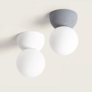 Puede incluir: Dos lámparas de techo blancas en forma de globo con una base de cerámica gris y blanca.