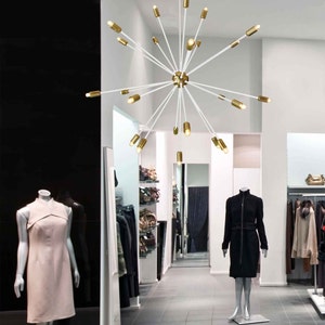 May include: A white modern chandelier with gold accents and multiple light bulbs hanging from the ceiling in a retail store.
