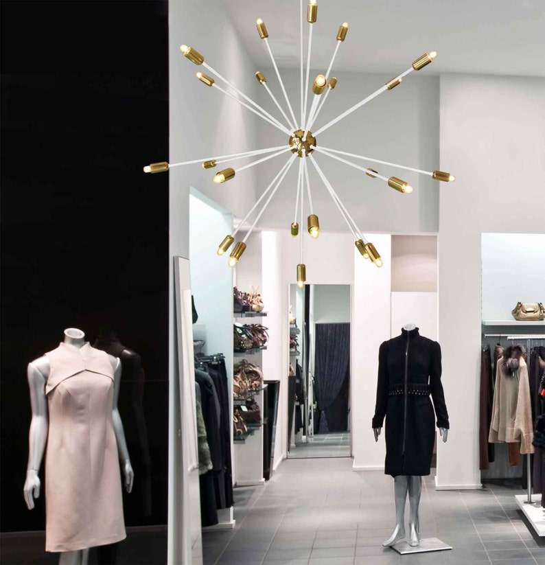May include: A white modern chandelier with gold accents and multiple light bulbs hanging from the ceiling in a retail store.