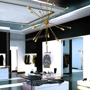 May include: A gold-toned, multi-arm chandelier with multiple light bulbs hangs from the ceiling of a modern retail store. The chandelier has a starburst design with long, thin arms extending outward from a central hub.