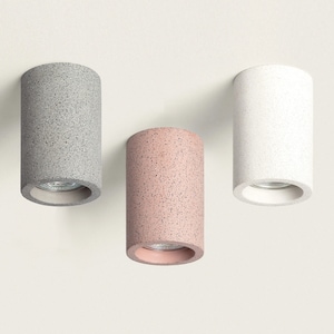 Op de afbeelding: Drie cilindrische plafondlampen in grijs, wit en roze met een gespikkelde afwerking.