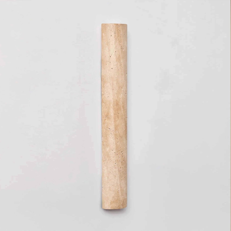 May include: A light beige, rectangular, stone-like object with a slightly textured surface. The object is a long, narrow column with a rounded end. The column is set against a white background.