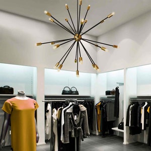 May include: A black and gold modern chandelier with multiple arms extending outward from a central point. The chandelier is hanging from the ceiling in a retail store setting.