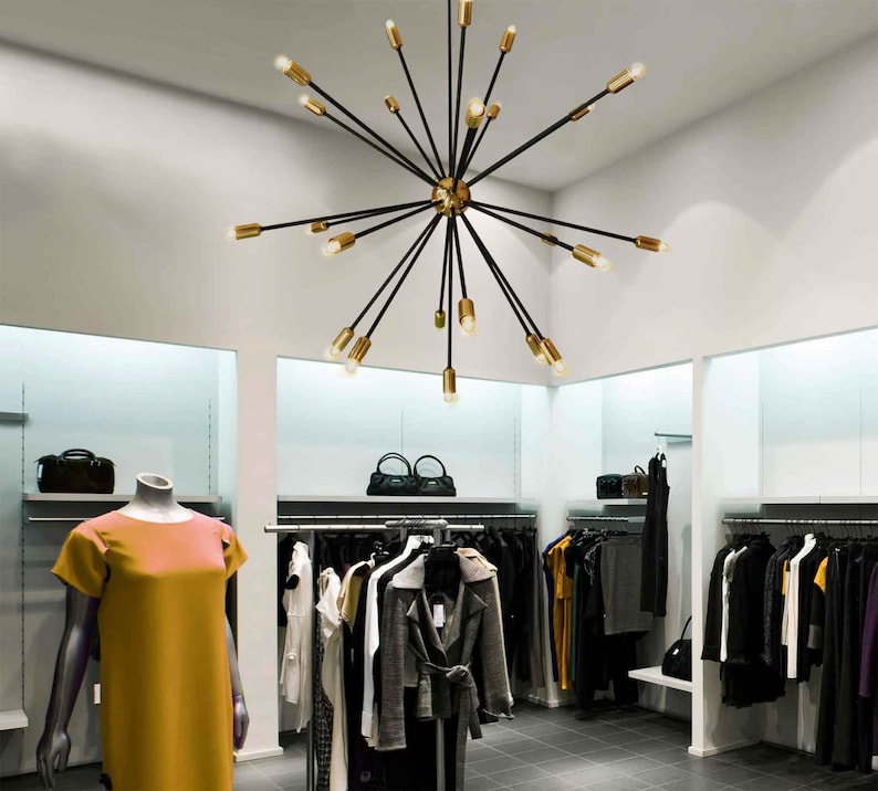 May include: A black and gold modern chandelier with multiple arms extending outward from a central point. The chandelier is hanging from the ceiling in a retail store setting.