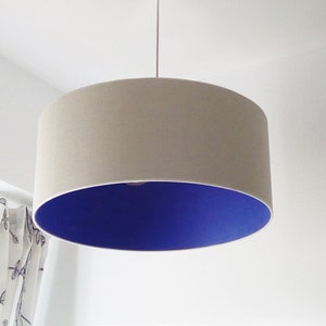 May include: A beige drum pendant light with a vibrant blue interior. The lampshade is cylindrical and suspended from the ceiling. The light fixture is a modern home decor item.