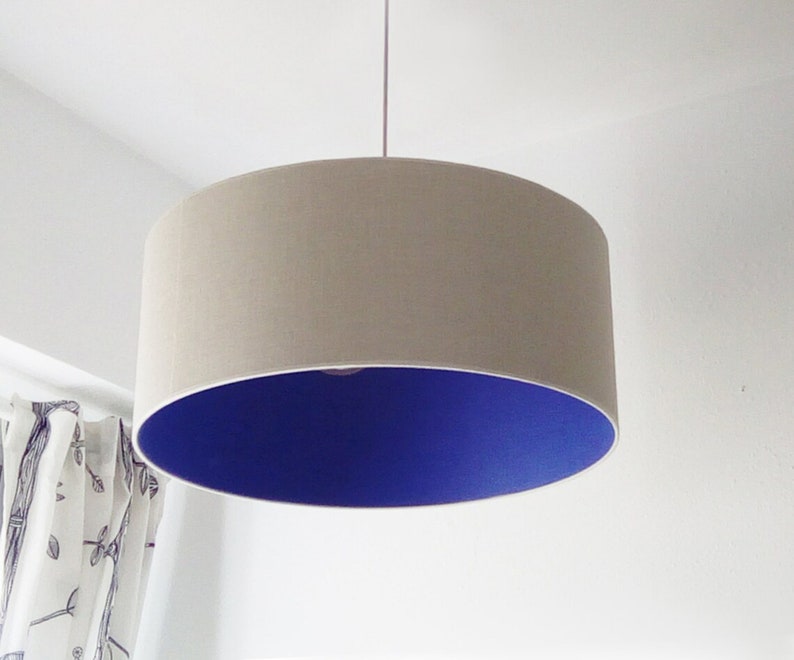 May include: A beige drum pendant light with a vibrant blue interior. The lampshade is cylindrical and suspended from the ceiling. The light fixture is a modern home decor item.