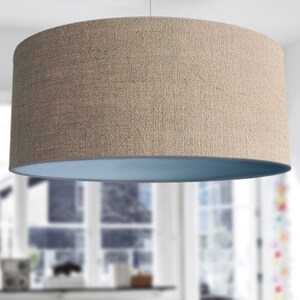 May include: A cylindrical lampshade with a textured, tan exterior and a light blue interior. The lampshade is suspended from the ceiling, showcasing a simple, modern design. The neutral colors and clean lines make it suitable for various interior styles.