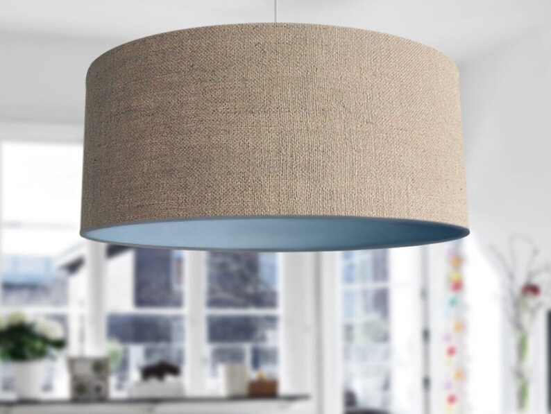 May include: A cylindrical lampshade with a textured, tan exterior and a light blue interior. The lampshade is suspended from the ceiling, showcasing a simple, modern design. The neutral colors and clean lines make it suitable for various interior styles.