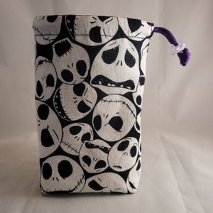 May include: A black and white fabric dice bag with a repeating pattern of Jack Skellington's face from the Nightmare Before Christmas. The bag has a purple drawstring with a clear plastic toggle.