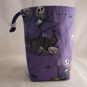 May include: Purple drawstring bag with a repeating pattern of Jack Skellington from The Nightmare Before Christmas. The pattern also includes bats, a graveyard, and a moon.