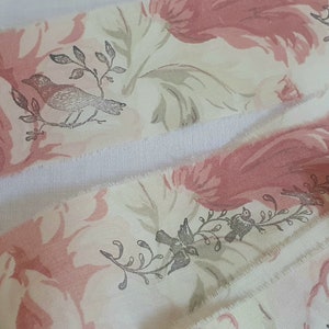 May include: A close-up of a pink and white floral ribbon with a grey bird design. The ribbon has a frayed edge and is folded in half.
