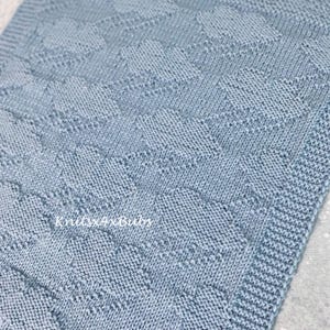 May include: A light blue knitted blanket featuring a repeating geometric pattern of raised diamond shapes and a textured border. The fabric has a consistent knit stitch throughout, and the text Knits4xBubs is printed in white on the surface.