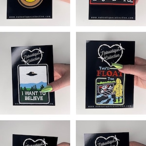 May include: Six embroidered iron-on patches on black cards with the Nabootique Collective logo. The patches feature various designs including a record with the words "Sick-Sap World", a text box with the words "The Lost Boys", a UFO with the words "I Want To Believe", a clown with the words "You'll Float Too", a Freddy Krueger glove with the words "Dream On", and a heart with a Jason Voorhees mask with the words "I 80's Horror".