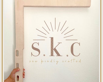 May include: A light wood shelf bracket with a cutout design. The bracket is held by a hand against a white wall. The text "S.K.C. sew kindly crafted" is printed below the bracket.