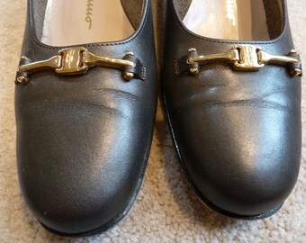 May include: A pair of black leather flats with gold buckles. The shoes have a rounded toe and a low heel.
