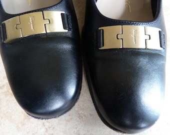 May include: A pair of black leather loafers with gold buckles. The buckles have the word "Ferragamo" engraved on them.