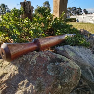 Peut inclure: Un rouleau à pâtisserie en bois artisanal avec une finition marron foncé. Le rouleau à pâtisserie est cylindrique avec une poignée arrondie à une extrémité et un trou à l'autre. Il repose sur une grosse pierre en extérieur.