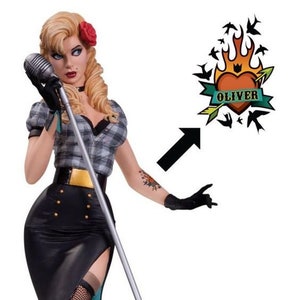 May include: A woman with blonde hair and red lipstick is holding a microphone. She is wearing a plaid shirt, a black skirt, and a belt with a gold buckle. She has a tattoo on her arm that says "Oliver" with a heart and an arrow.