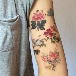 K&ouml;nnte beinhalten: Ein Arm mit einem floralen Tattoo. Das Tattoo zeigt mehrere rosa, rote und wei&szlig;e Blumen mit gr&uuml;nen Bl&auml;ttern.