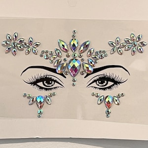 May include: A sheet of iridescent face jewels in the shape of stars and teardrops. The jewels are arranged in a design that can be applied to the forehead and around the eyes.