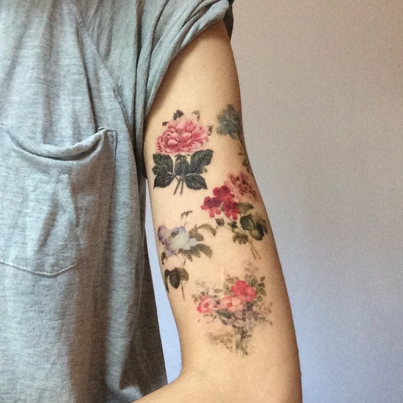 K&ouml;nnte beinhalten: Ein Arm mit einem floralen Tattoo. Das Tattoo zeigt mehrere rosa, rote und wei&szlig;e Blumen mit gr&uuml;nen Bl&auml;ttern.