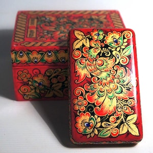 Könnte beinhalten: Zwei rote lackierte Schachteln mit aufwendigen Blumenmustern in Gold, Grün und Orange. Die rechteckige Schachtel ist geöffnet und zeigt eine kleinere Schachtel mit einem ähnlichen Muster. Die Schachteln sind wahrscheinlich dekorativ oder zur Aufbewahrung.