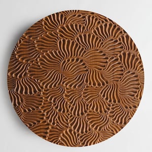 May include: A round wooden coaster featuring a carved pattern of overlapping, organic shapes. The coaster is a rich brown colour.