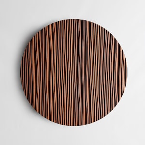 Puede incluir: Una decoración de pared redonda de madera con un patrón ondulado y rayado en tonos marrones y negros.