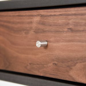 May include: Close-up of a wooden drawer with a silver knob. The drawer is made of walnut wood and has a natural finish.