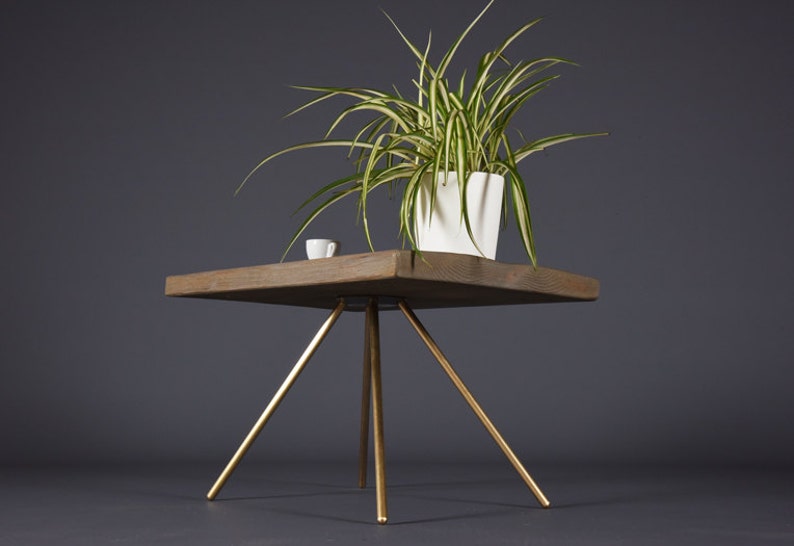 May include: A square wooden table with a gold metal tripod base. A potted plant with green and white leaves sits on the table.