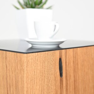 May include: A wooden end table with a black glass top. The table has a small, rectangular cutout on the front.