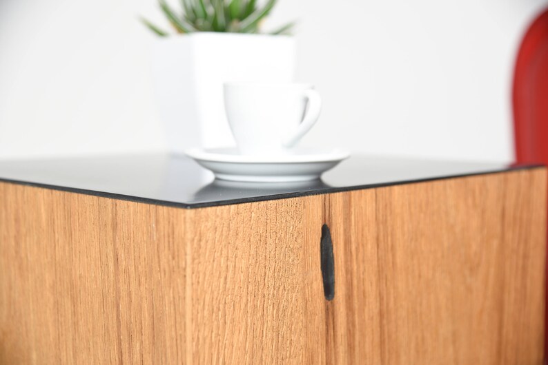 May include: A wooden end table with a black glass top. The table has a small, rectangular cutout on the front.