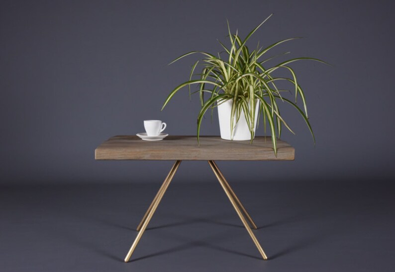 May include: A wooden coffee table with a gold metal tripod base. A white ceramic cup and saucer and a potted plant are on the table.