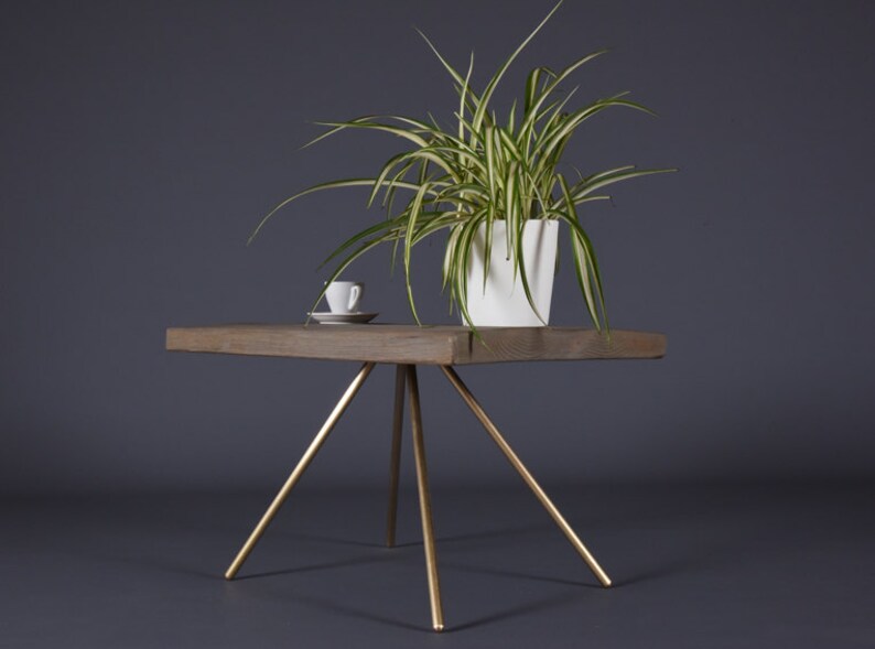 May include: A wooden coffee table with a gold metal tripod base. A white ceramic cup and saucer and a potted plant are on the table.