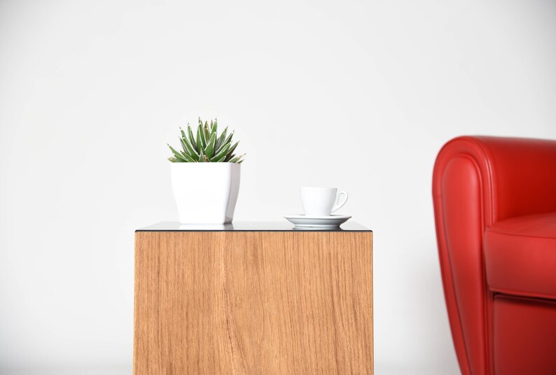 May include: A small potted succulent plant sits on a wooden end table with a white cup and saucer. A red armchair is in the background.