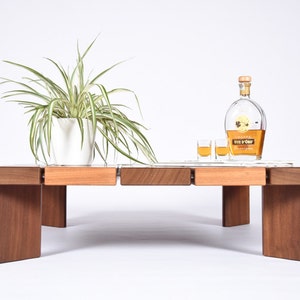 May include: A wooden coffee table with a light wood top and dark wood legs. The table has a white ceramic plant pot with a green plant on it. There are two small glasses and a bottle of Vin d'Or liqueur on the table.