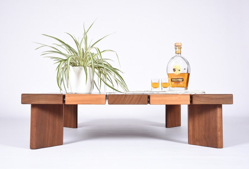 May include: A wooden coffee table with a light wood top and dark wood legs. The table has a white ceramic plant pot with a green plant on it. There are two small glasses and a bottle of Vin d'Or liqueur on the table.
