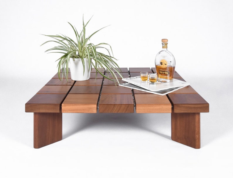 May include: A wooden coffee table with a grid-like design. The table is made of multiple square pieces of wood that are joined together. There is a plant in a white pot, a bottle of liquor, and shot glasses on the table.