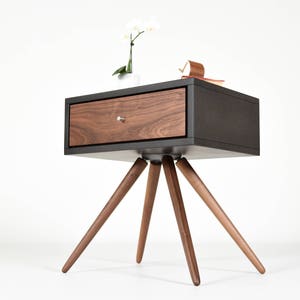 May include: A black nightstand with a walnut drawer and four wooden legs. The nightstand has a modern design and is perfect for a bedroom.