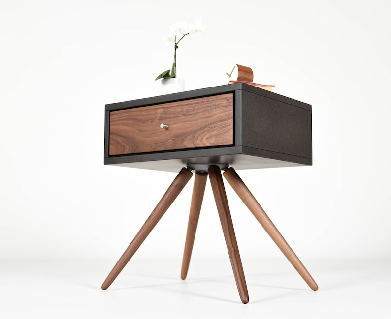 May include: A black nightstand with a walnut drawer and four wooden legs. The nightstand has a modern design and is perfect for a bedroom.