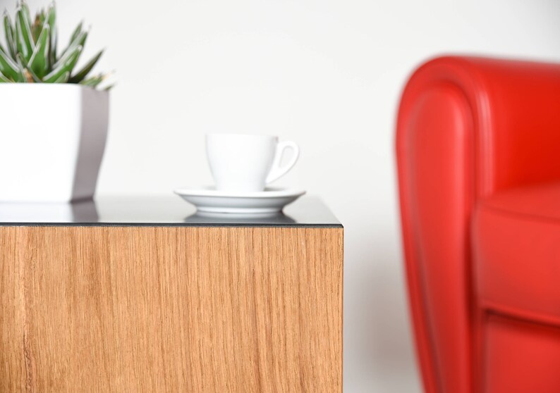 May include: A wooden end table with a glass top. A white coffee cup and saucer are on the table. A red armchair is in the background.