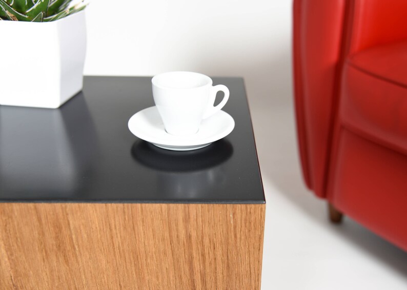 May include: A black and wood end table with a white cup and saucer on top. The table has a black top and a wood base.