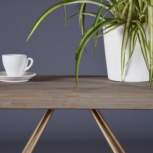 May include: A white ceramic coffee cup and saucer sit on a wooden table with a gold metal base. A potted plant with green and white striped leaves is in the background.