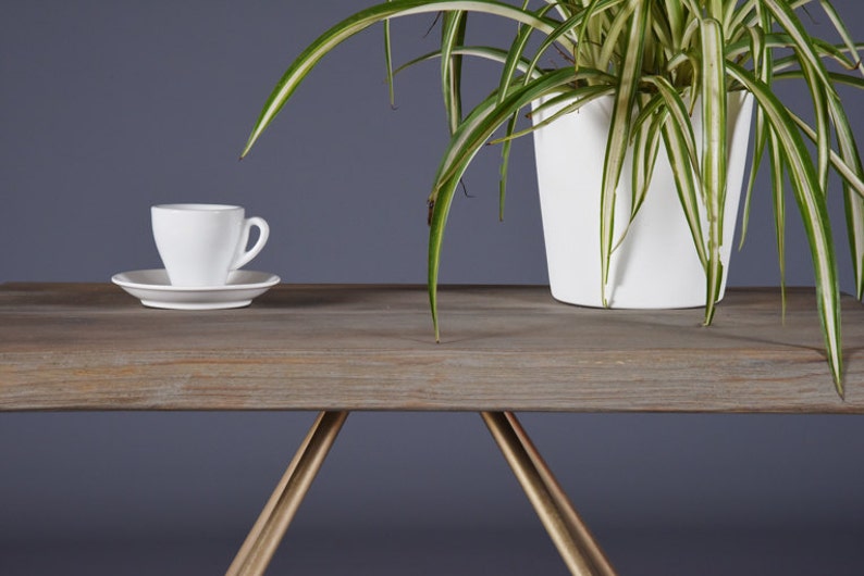 May include: A white ceramic coffee cup and saucer sit on a wooden table with a gold metal base. A potted plant with green and white striped leaves is in the background.
