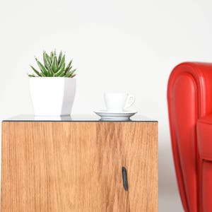 May include: A wooden side table with a glass top. A small white potted succulent plant sits on the table next to a white cup and saucer.
