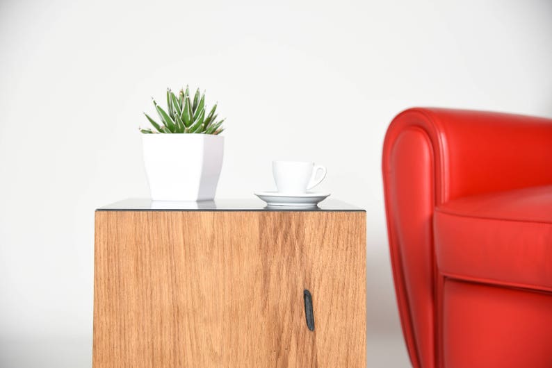 May include: A wooden side table with a glass top. A small white potted succulent plant sits on the table next to a white cup and saucer.