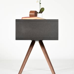 May include: A dark gray side table with a rectangular top and three wooden legs. The table is made of wood and has a modern design.