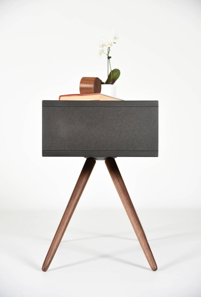 May include: A dark gray side table with a rectangular top and three wooden legs. The table is made of wood and has a modern design.