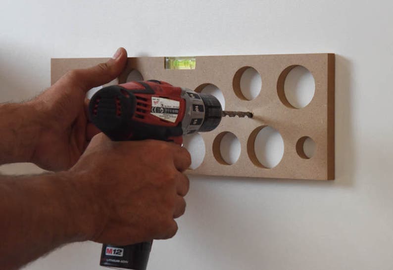 May include: A person is using a red and black power drill to drill holes in a piece of wood with a level attached to the top.